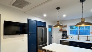 Cocina moderna con una isla central, armarios azul oscuro, electrodomésticos de acero inoxidable, iluminación colgante y un amplio ventanal con vistas al exterior.