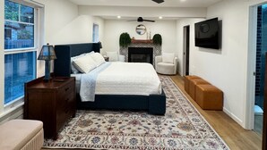 Un dormitorio con cama, ventilador de techo, chimenea, televisor y ventana.