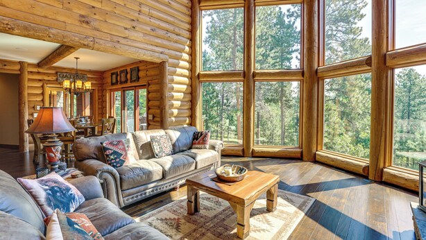 A log cabin interior with a large window, a sofa, a coffee table, and a chandelier. - Hike, Fish & More: Grand Cabin w/ Decks in Sturgis (Sturgis)