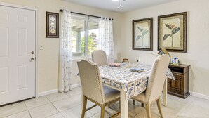 Un coin repas avec une table dressée pour quatre personnes, des chaises, un ventilateur de plafond et une fenêtre avec des rideaux.
