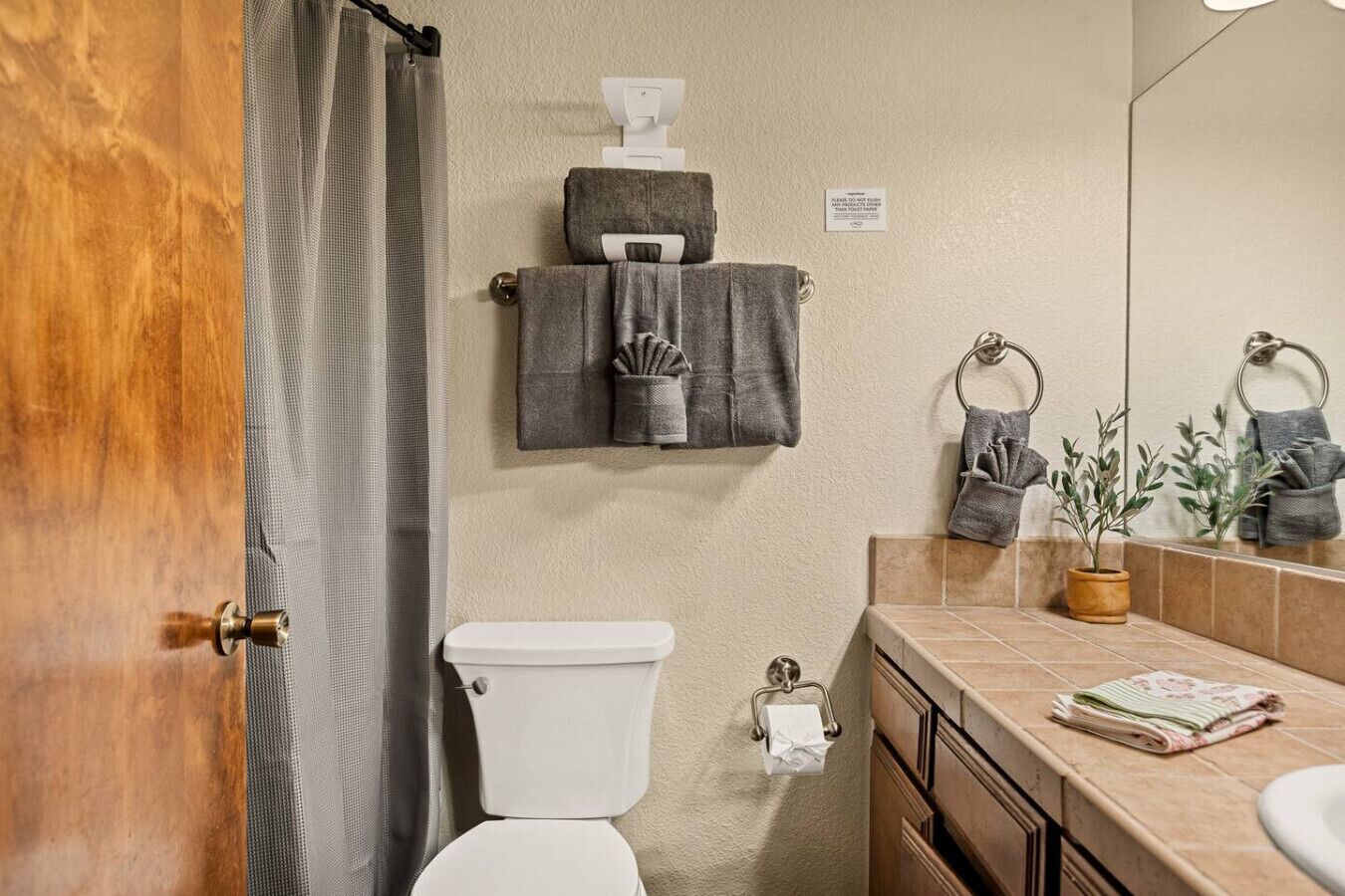 A bathroom with a toilet, a towel rack with towels, a mirror, and a sink with a plant.