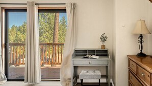 Une pièce avec une porte-fenêtre coulissante donnant sur une terrasse, un petit bureau avec une lampe et une commode en bois.