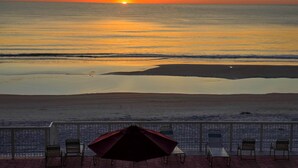 A beach view with a sunset, chairs, and an umbrella on a patio. - Pool, Balcony & More! Oceanfront Shores Club Condo (Daytona Beach Shores)