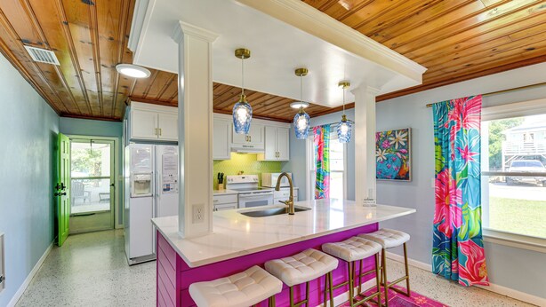Una cocina con una isla central, taburetes de bar, un refrigerador y un microondas.