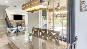 A spacious dining area with a large glass table, wooden chairs, and a modern chandelier.