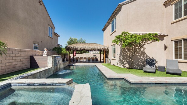 A clear swimming pool with a stone edge, a thatched-roof structure, and two lounge chairs.