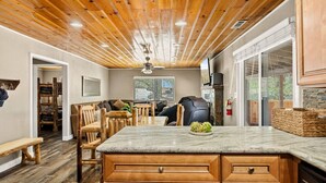 A modern kitchen with a wooden ceiling, a marble countertop, and a dining area with wooden chairs and a bench. - Lawliss Hideout, Steps to Village w/ Hot Tub (Big Bear Lake)
