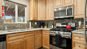 A kitchen with wooden cabinets, a stainless steel stove, a microwave, and a red kettle. - Lawliss Hideout, Steps to Village w/ Hot Tub (Big Bear Lake)