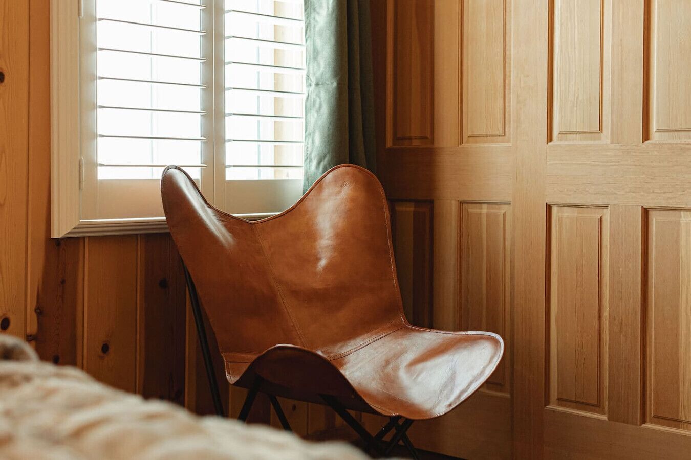 Ein Zimmer mit Holztür, einem Fenster mit Jalousien und einem braunen Ledersessel.