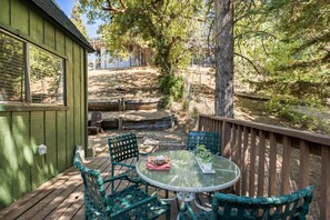 A wooden deck with a glass table and chairs, surrounded by trees and a wooden fence. - Casa Huntsted A-Frame Cabin near Snow Valley (Running Springs)
