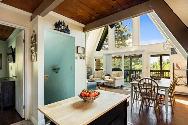 A spacious dining area with a wooden table and chairs, a view of the outdoors, and a door leading to another room. - Casa Huntsted A-Frame Cabin near Snow Valley (Running Springs)