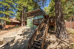 A wooden staircase leading to a green cabin with a balcony, surrounded by trees. - Casa Huntsted A-Frame Cabin near Snow Valley (Running Springs)