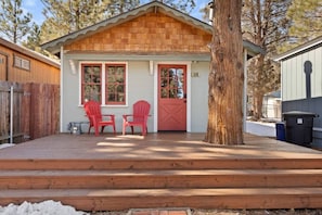 Une petite cabane en bois avec une véranda, deux chaises Adirondack rouges et une porte rouge.