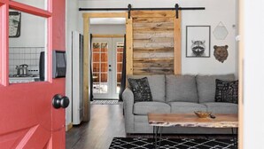 Een woonkamer met een grijze bank, een houten tafel, een rode deur en een schuifdeur in boerderijstijl.