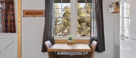 A dining area with a wooden table and chairs, a window with curtains, and a 'WELCOME' sign.