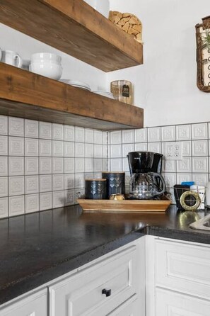 Une cuisine avec des armoires blanches, un comptoir noir et une étagère en bois sur laquelle sont disposés divers objets.