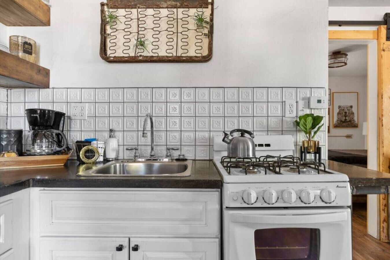 A kitchen with white cabinets, a gas stove, a coffee maker, and a decorative wall piece.