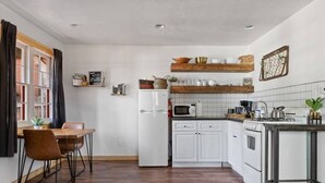 Een compacte keuken met witte kasten, een houten eettafel en een kleine bar.