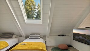Camera da letto con due letti, un velux, una televisione e vista sugli alberi.