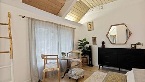 Una stanza con soffitto in legno, un comò nero, un tavolo rotondo con sedie, un grande specchio e una pianta.