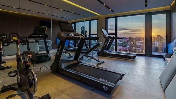 Un gimnasio moderno con cintas de correr y bicicletas estáticas, amplias ventanas con vista a la ciudad.