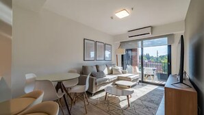 Una sala de estar moderna con un sofá, una mesa de comedor con sillas, un televisor y un balcón con vistas.