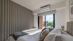 Un dormitorio moderno con una cama grande, vistas al balcón por una puerta corredera y un aire acondicionado de pared.