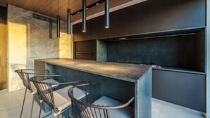 Una cocina moderna con una isla central, taburetes de bar, iluminación colgante y muebles oscuros.