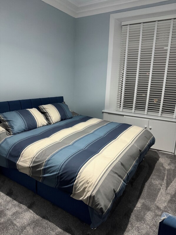 Een slaapkamer met een bed, een raam met zonwering en een vloerbedekking.