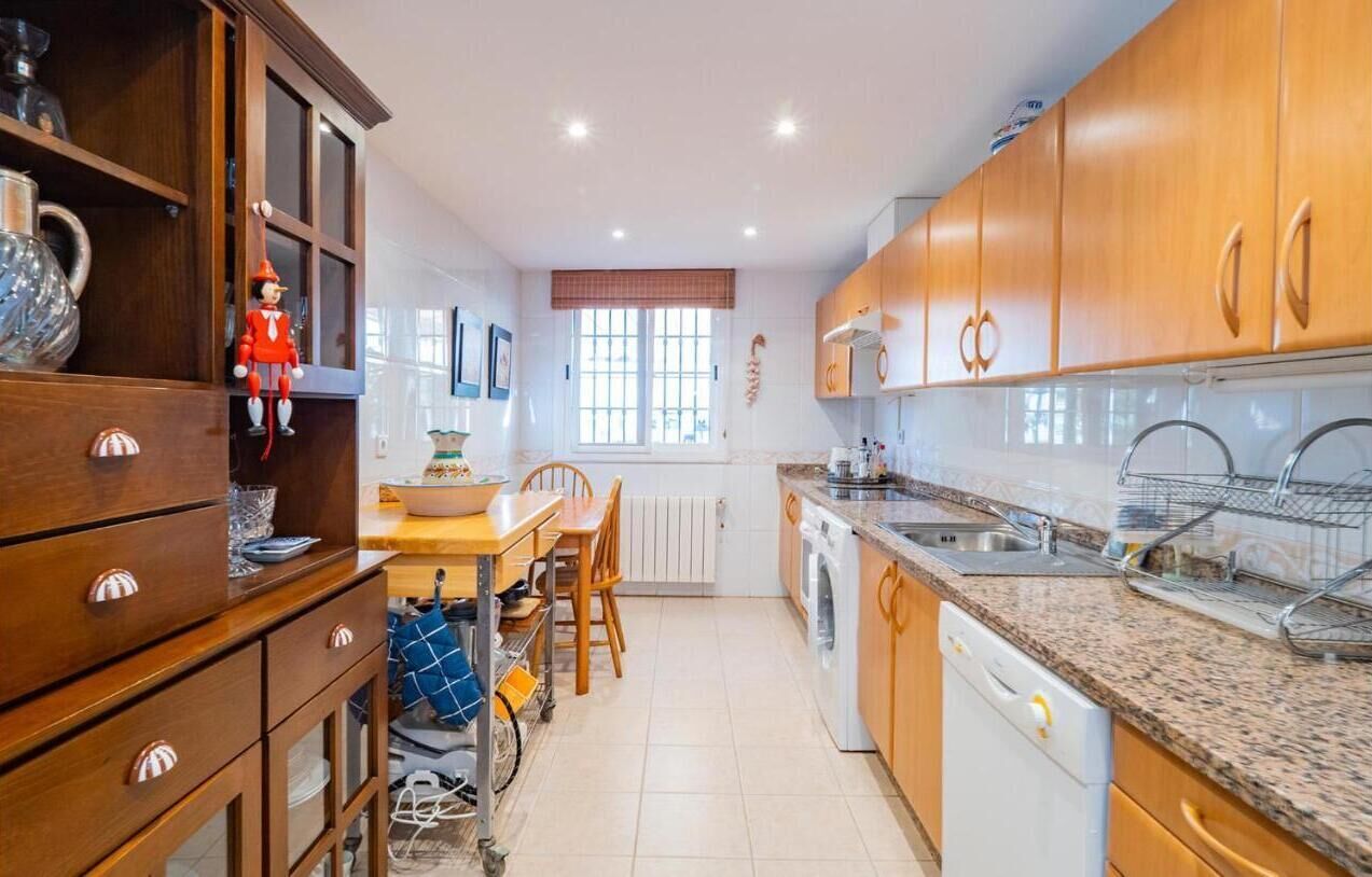 Una cocina con armarios de madera, horno empotrado, lavabo y comedor con mesa y sillas.