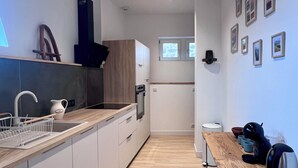 Moderni keittiö, jossa on puiset kaapit, sisäänrakennettu uuni ja pesuallas. Keittiössä on puinen pöytä, jonka päällä on vedenkeitin ja kuppeja.