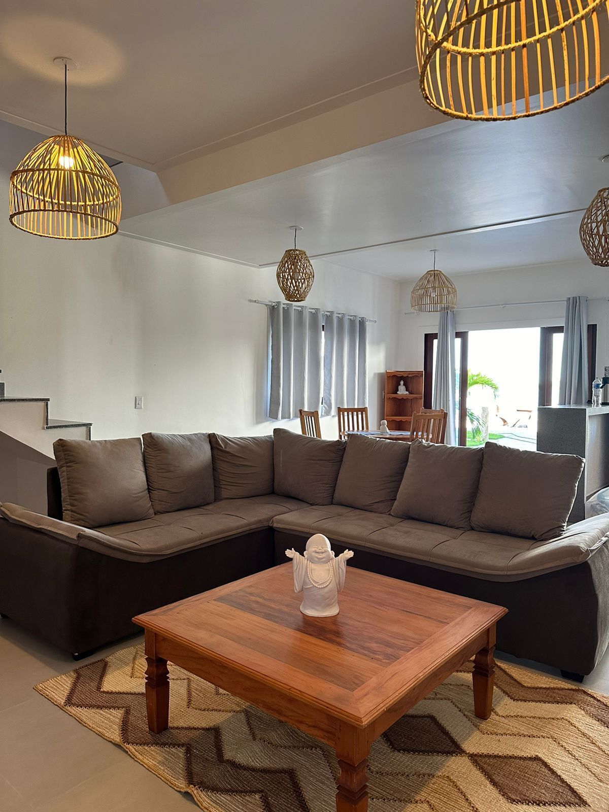 Een moderne woonkamer met een hoekbank, een houten salontafel en drie hangende rieten lampen.