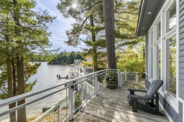A wooden deck with a railing overlooking a lake, surrounded by trees.