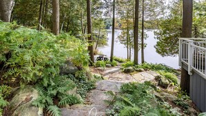 Una escalera de piedra que conduce a un muelle junto a un lago, rodeado de helechos y árboles.