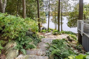 Una escalera de piedra que conduce a un muelle junto a un lago, rodeado de helechos y árboles.