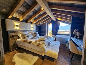 A bedroom with a large bed, a wooden ceiling, a window with a view, and a bathtub.