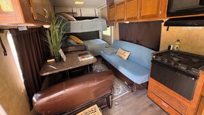A compact RV interior with a kitchenette, a sofa, a table, and a bench.