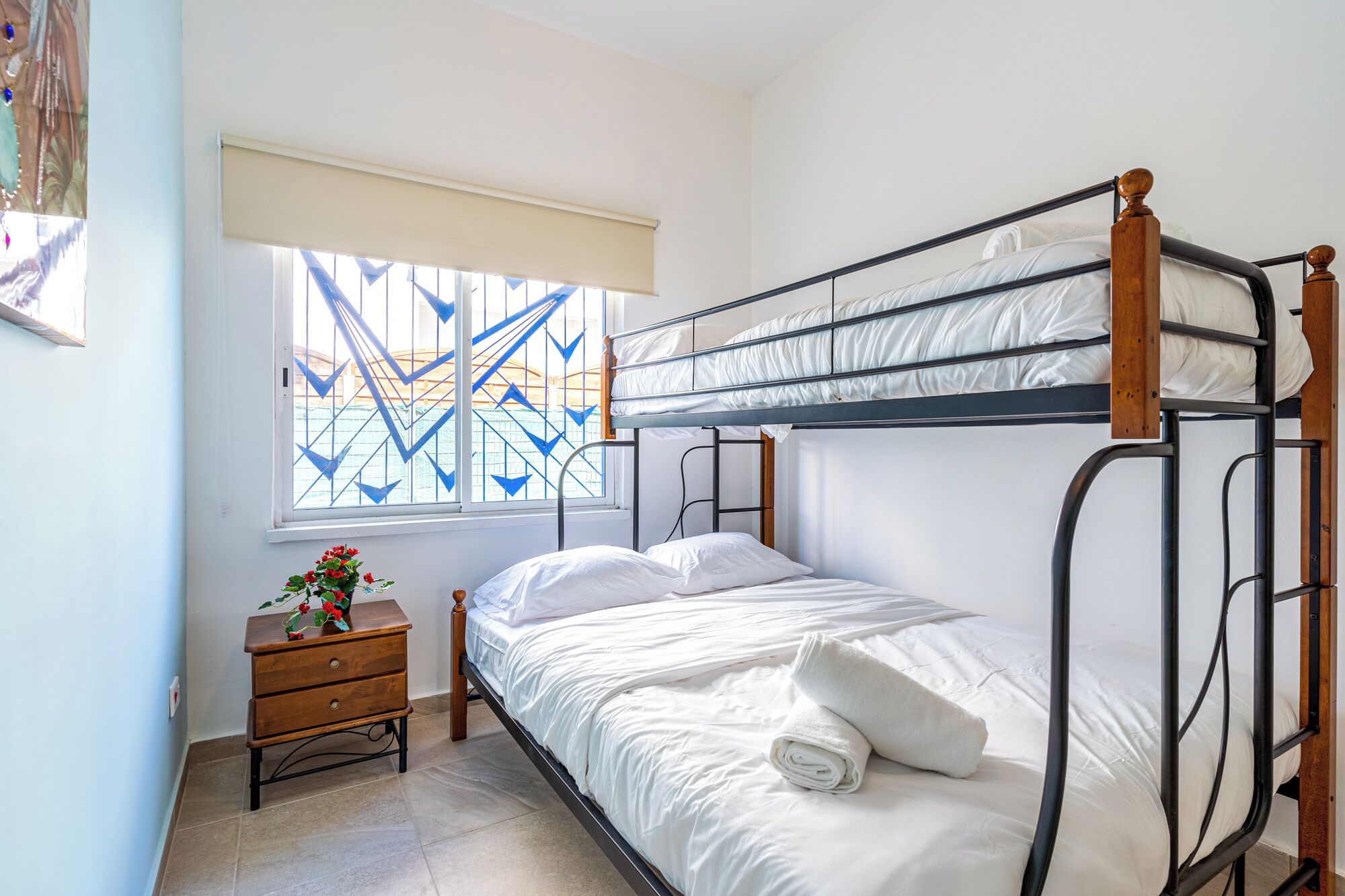 Une chambre avec un lit superposé, une table de chevet en bois et une fenêtre ornée d’un motif géométrique.