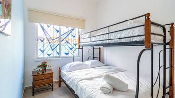 Une chambre avec un lit superposé, une table de chevet en bois et une fenêtre ornée d’un motif géométrique.