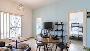 A modern living room with a dining table, chairs, a sofa, a TV, and a bed in the background. - Nala - 2 Bedroom Apt & Patio in Larnaca (Larnaca)