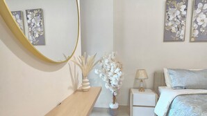 A bedroom with a large mirror, a bedside table, a lamp, a bed with a patterned duvet, and two floral wall art pieces.