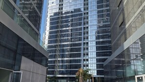 A modern building with reflective glass facade, a spacious courtyard, and a palm tree.