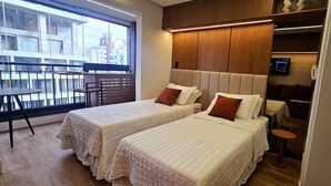 Een hotelkamer met twee bedden, een tafeltje en uitzicht op de stad door grote ramen.