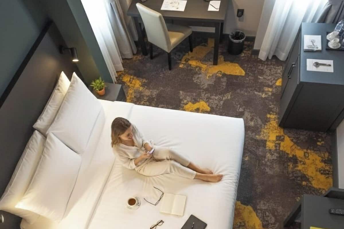 A hotel room with a bed, a desk, a chair, and a small table with a plant.
