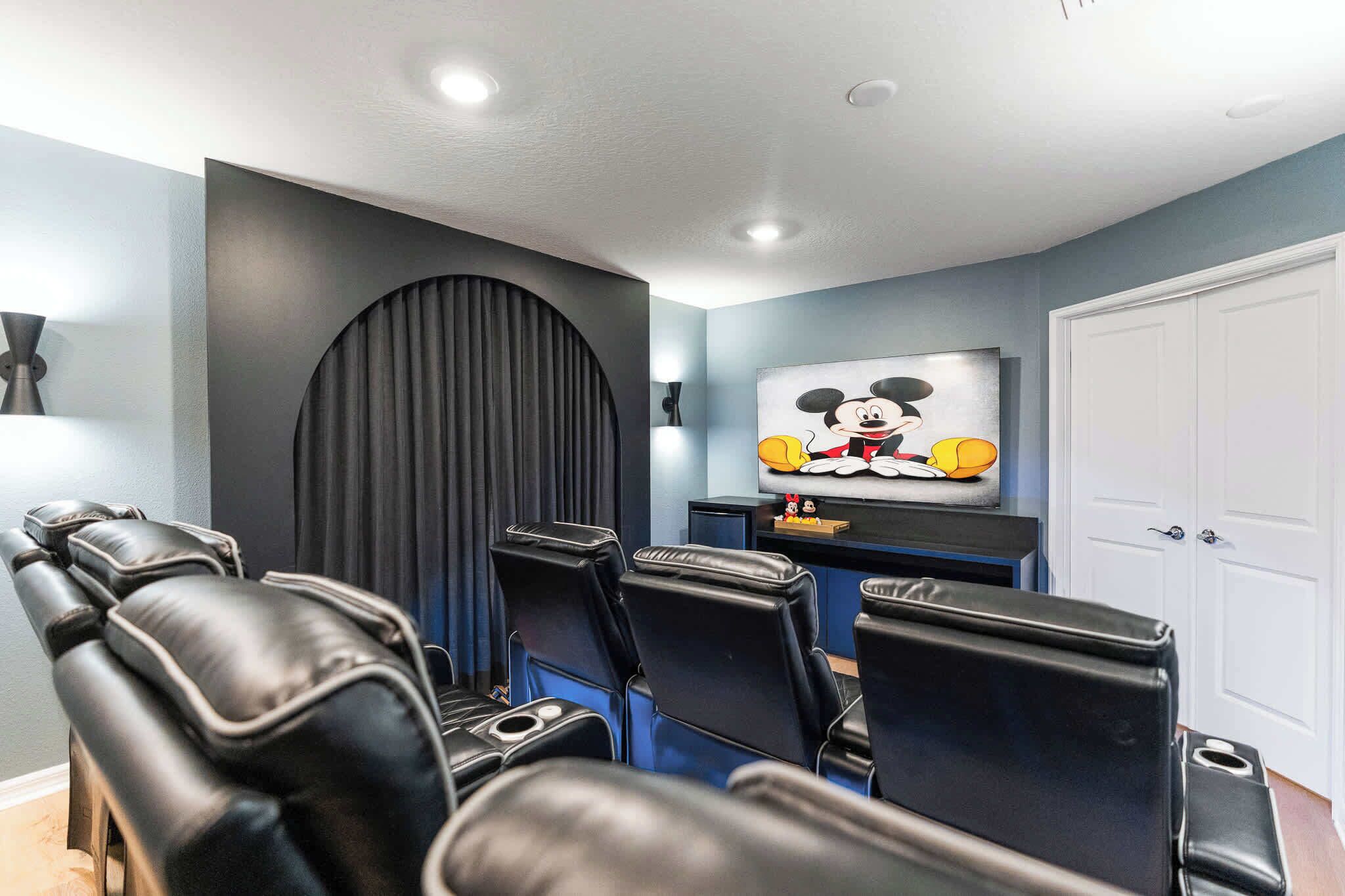 A room with a large black wall, a Mickey Mouse painting, and several black leather chairs.