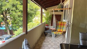 Un balcon avec un hamac, un fauteuil rembourré et une vue sur les arbres et les voitures garées.