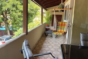 Ein Balkon mit einer Hängematte, einem gepolsterten Stuhl und Blick auf Bäume und parkende Autos.