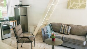 Un espace de vie compact comprenant un coin cuisine, un canapé, une table à manger et une échelle adossée au mur.