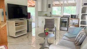 Un salon moderne doté d’un téléviseur à écran plat, d’un canapé, d’une table basse agrémentée d’une plante en pot, et d’un coin cuisine avec une cuisinière et un four à micro-ondes.