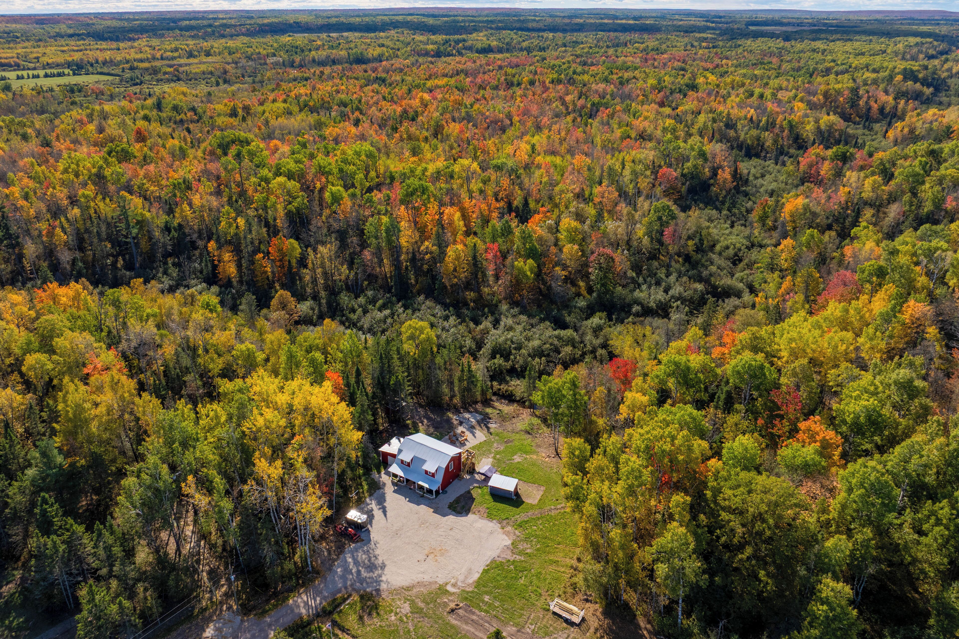 An aerial view of a red barn with a white roof surrounded by a forest.